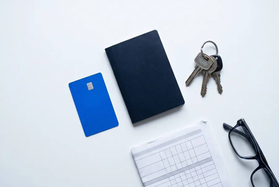 Blue card, booklet, keys and glasses on a white desk